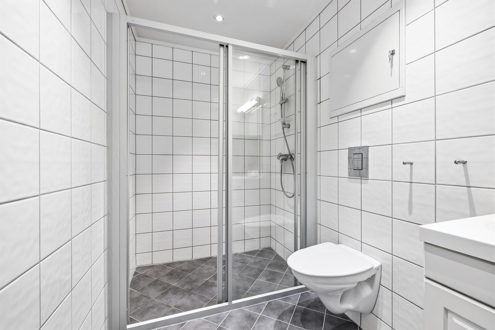 Bad med lyse og tidløse fliser, vegghengt dusj og servant med underskap. Varme i gulv. Galleribilde