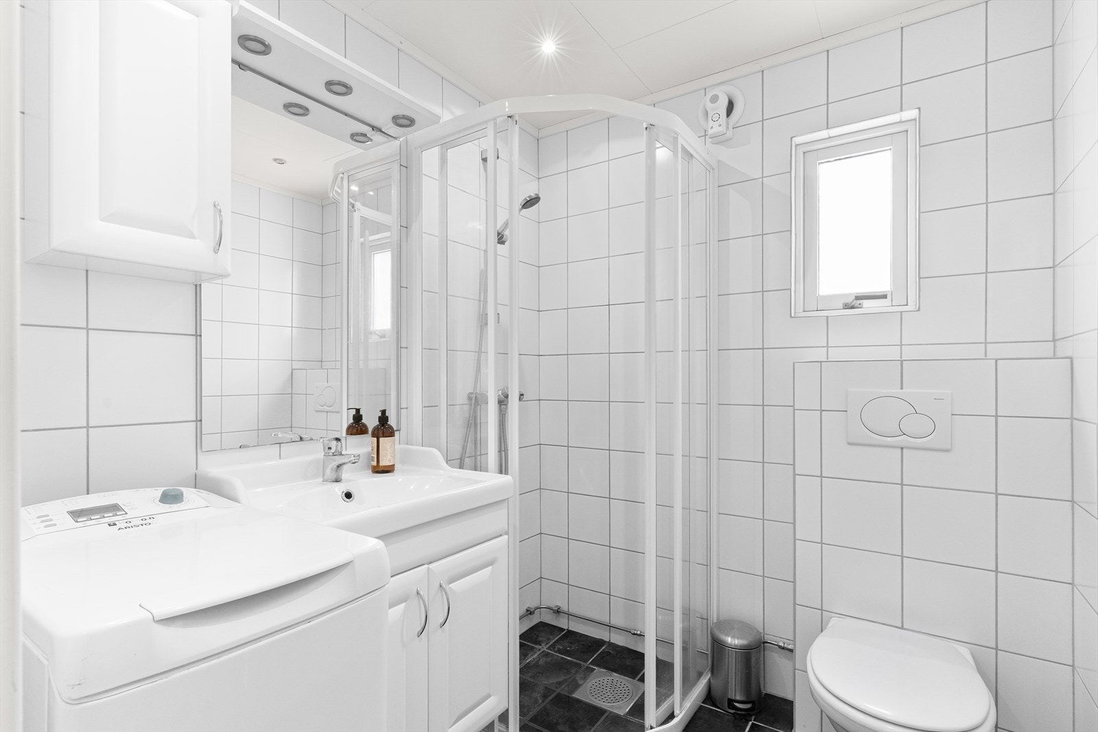 Lyst og pent flislagt bad med varmekabler i gulv. Rommet har innredning med nedfelt servant, veggmontert toalett, dusjvegger/hjørne og opplegg for vaskemaskin. Galleribilde