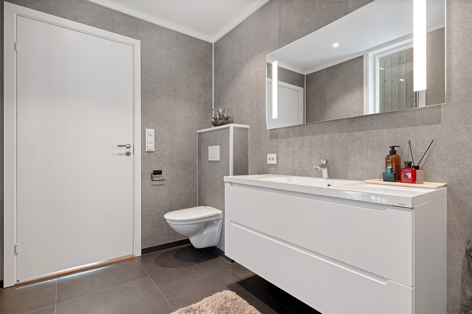 Badet er innredet med baderomsinnredning, veggmontert toalett og dusjhjørne med innfellbare dører Galleribilde