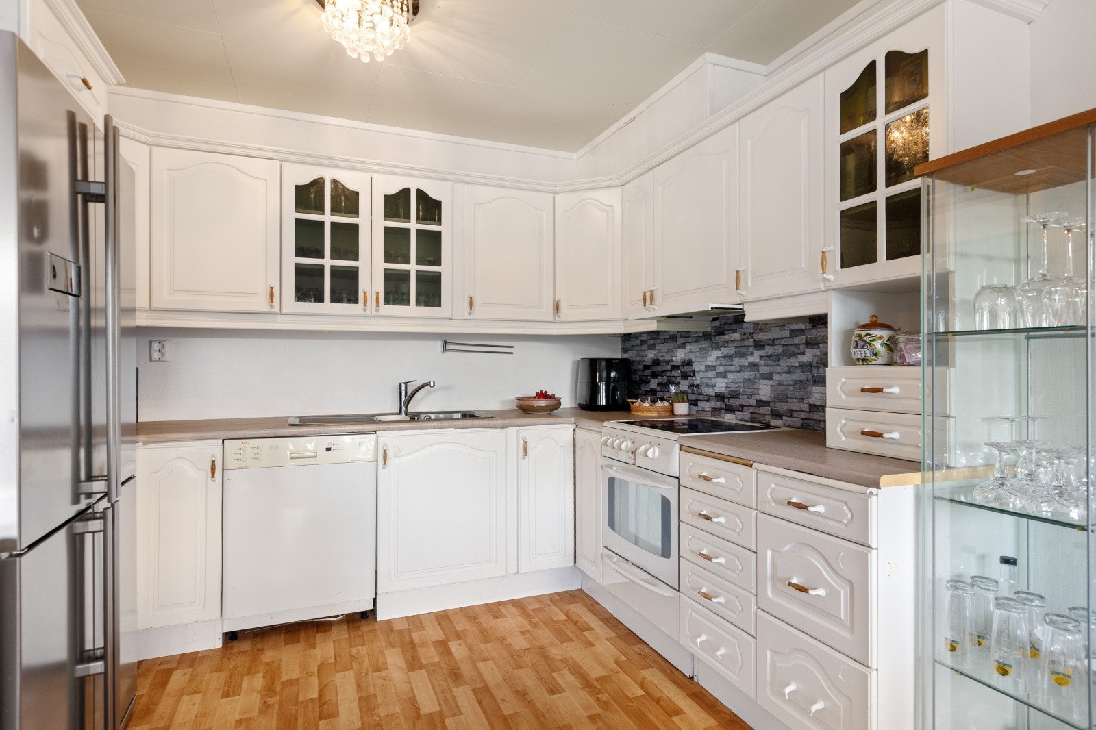 Klassisk kjøkkeninnredning med hvitevarer som komfyr, oppvaskmaskin og kombinert kjøl/frys som følger boligen. Galleribilde