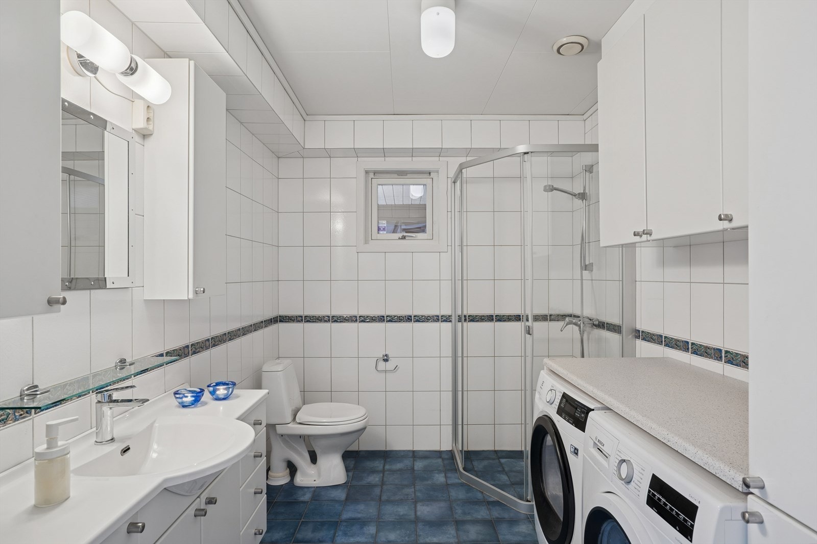 Badet i 1.etg har varmekabler i gulvet. Innredet med servantseksjon, gulvmontert toalett og dusjhjørne. Det er opplegg for vaskemaskin. Galleribilde