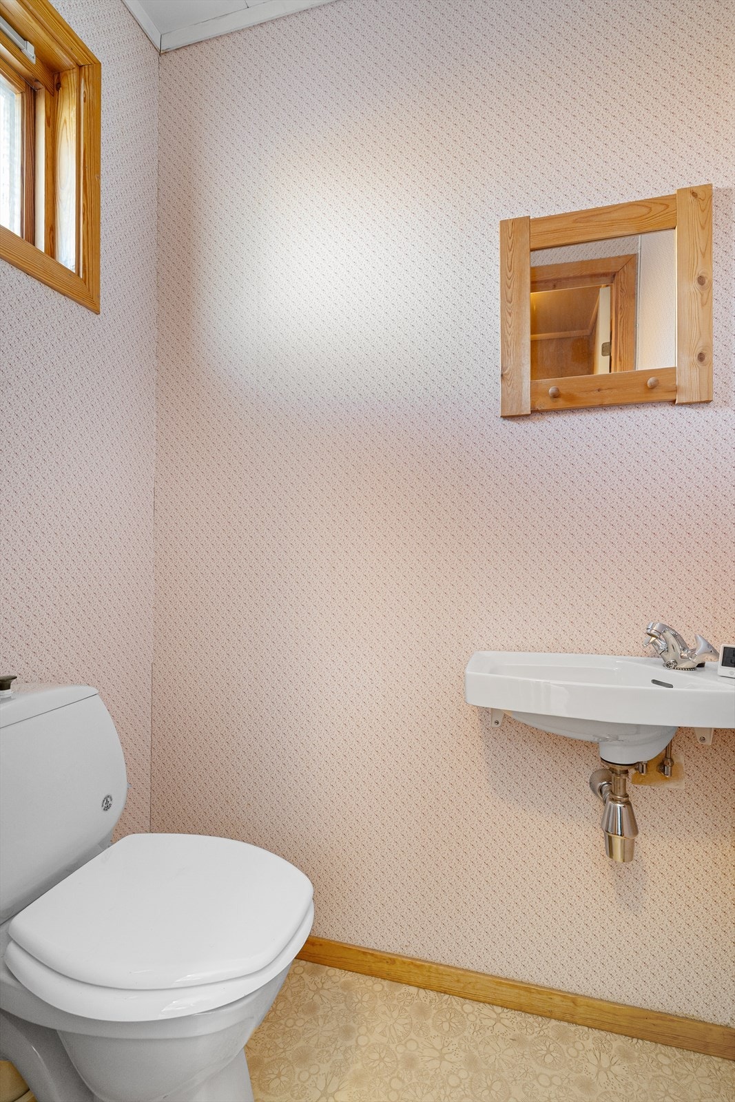 Boligen har eget gjestetoalett beliggende inntil entrèen, med gulvmontert toalett og enkel servant. Overflater her er belegg på gulvet og tapet på veggene. Galleribilde