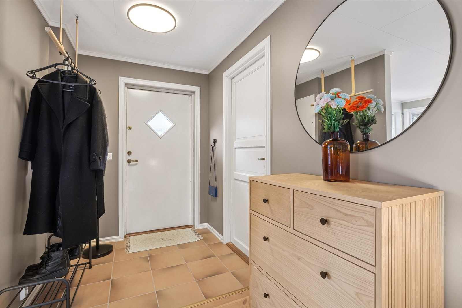 Videre innenfor inngangsdøren ønsker en hyggelig gang deg velkommen inn. Rommet er pent gjennomført med flislagt gulv og lyse farger på vegger og tak. Det er god plass til å både henge og sette fra seg sko og yttertøy. Galleribilde