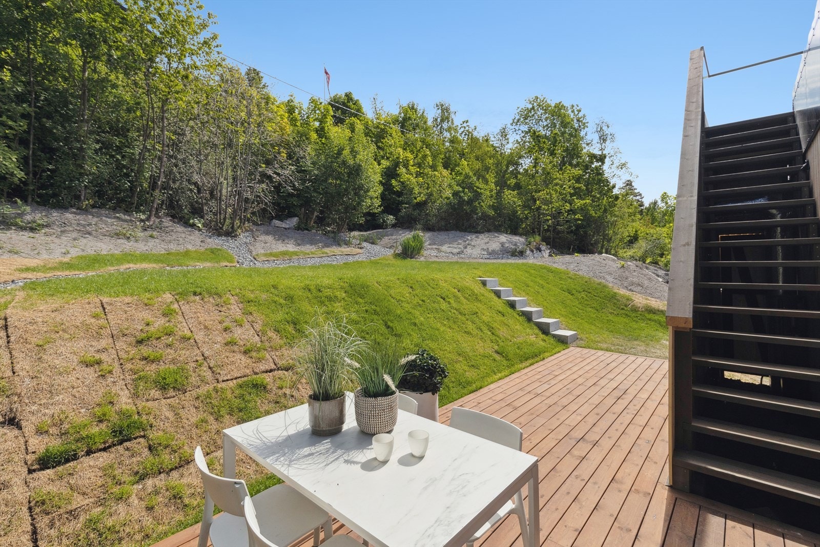 Fra terrassen på baksiden er trapp opp til takterrassen. Tomten er pent opparbeidet med plen Galleribilde