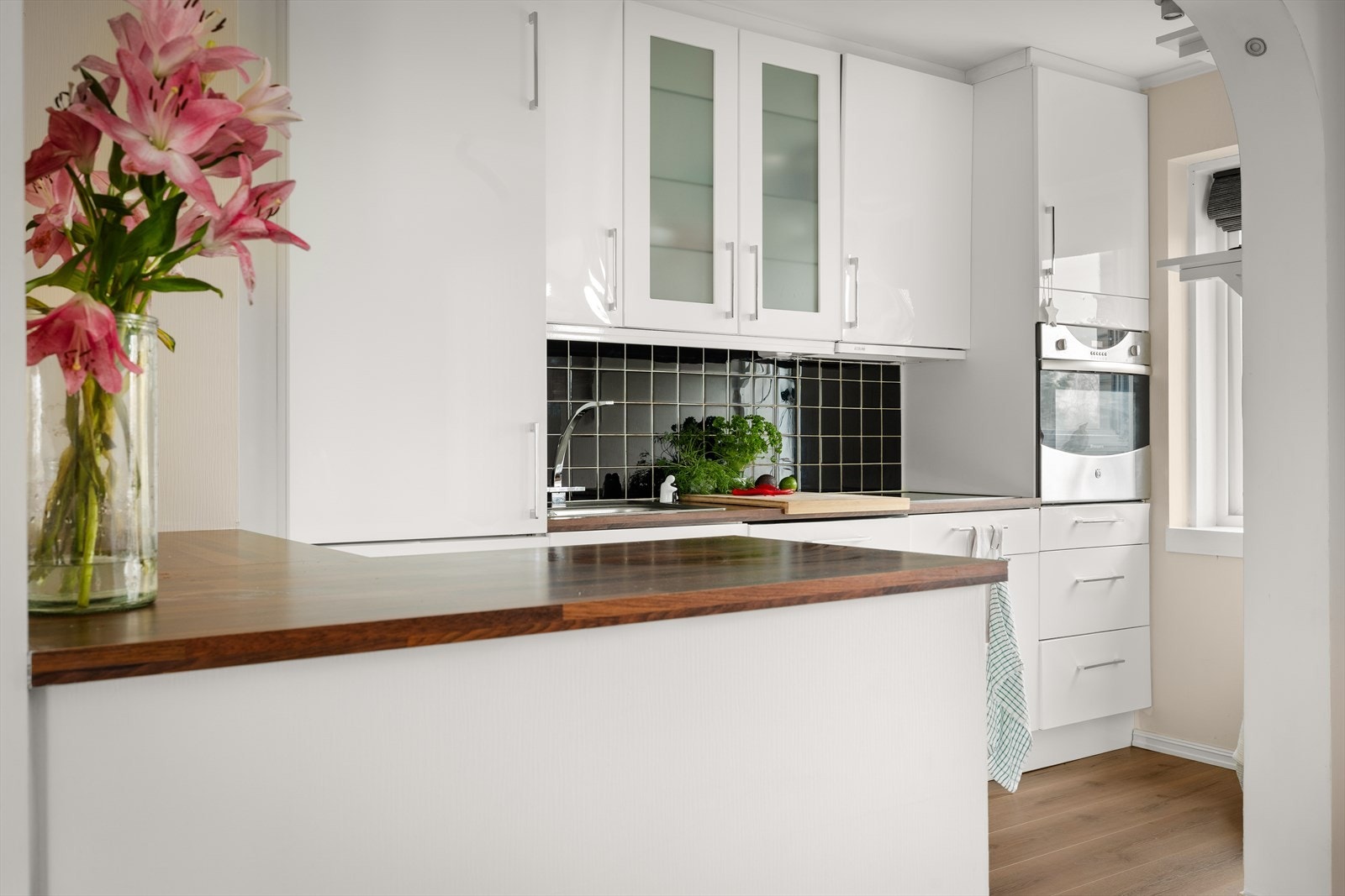 Kjøkkenet har lyse slette fronter, laminert benkeplate og oppvaskkum. Det er fliser mellom benk og overskap. Galleribilde