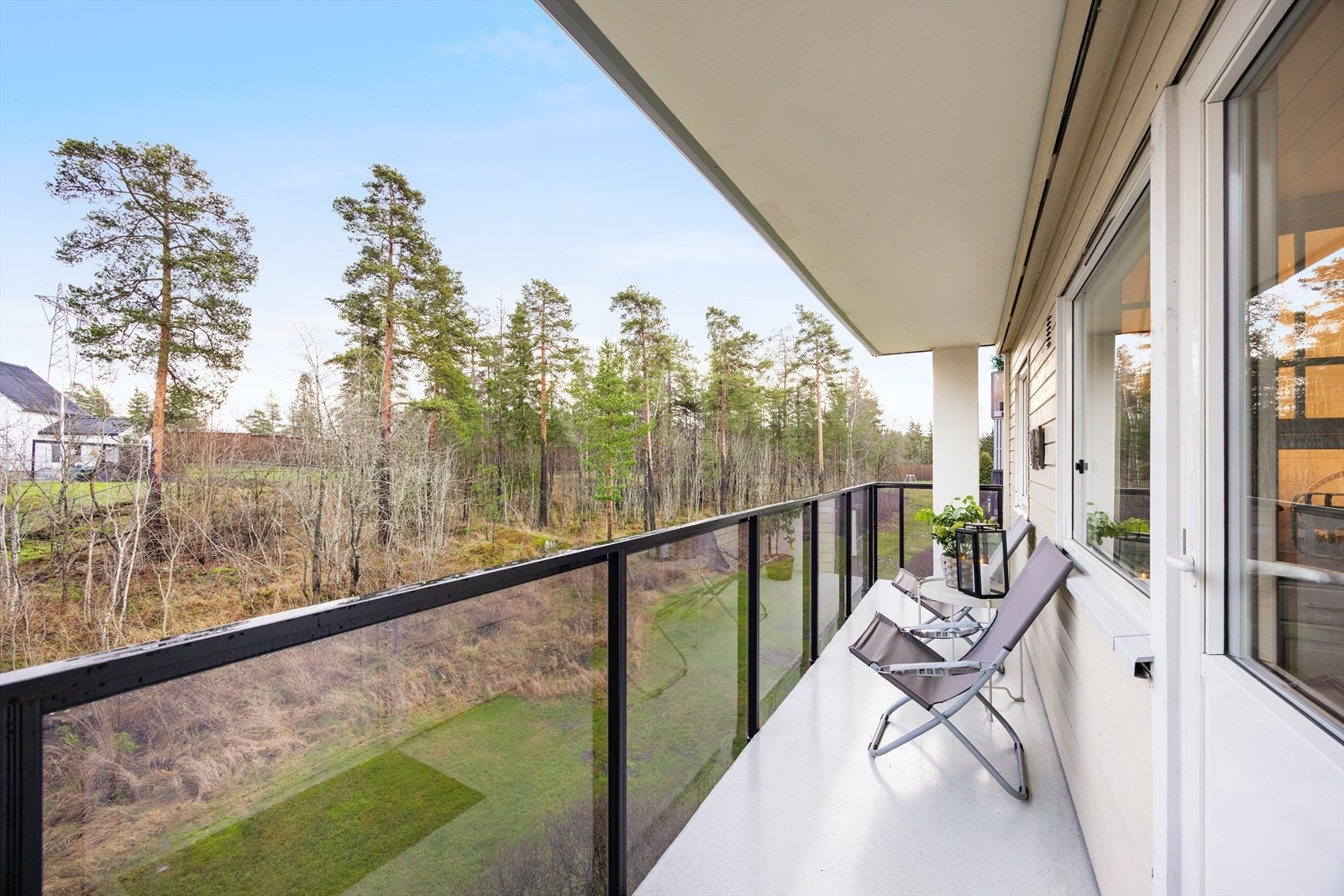 Balkongen har rekkverk i metall med glassfelt og utsikt mot grønne fellesarealer. Galleribilde