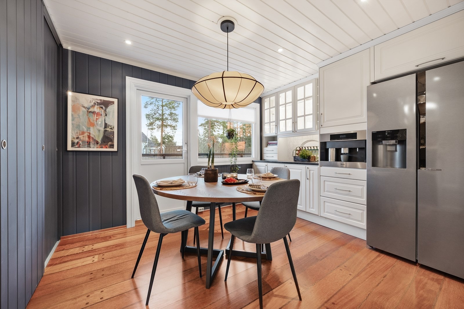 Et velutstyrt kjøkken med profilerte fronter, integrerte hvitevarer og en hyggelig spiseplass ved vinduet. Galleribilde