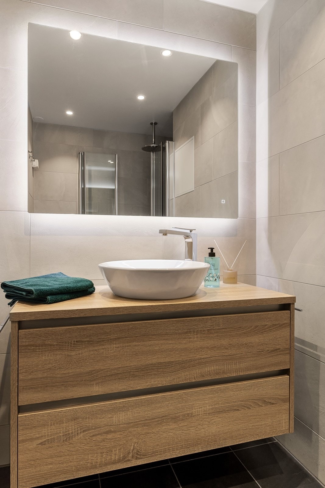 Rommet har en pen baderomsinnredning med skuffer og toppmontert servant med ett-greps blandebatteri. Speil med lys på vegg over servanten.r Galleribilde