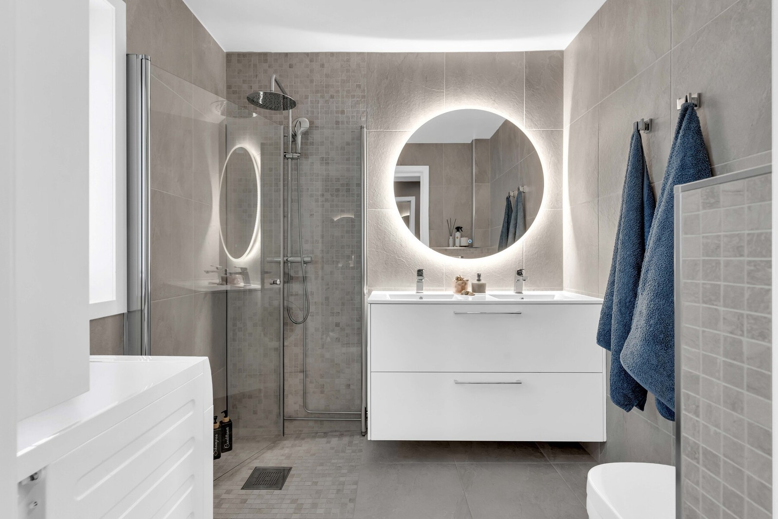 Svært stilrent bad med flislagt gulv med varme, helfliset vegger og malt himling. Rommet er innredet med dusjhjørne med glassdører, servantskap med servant, speil med belysning og vegghengt toalett. Det er også opplegg for vaskemaskin. Galleribilde