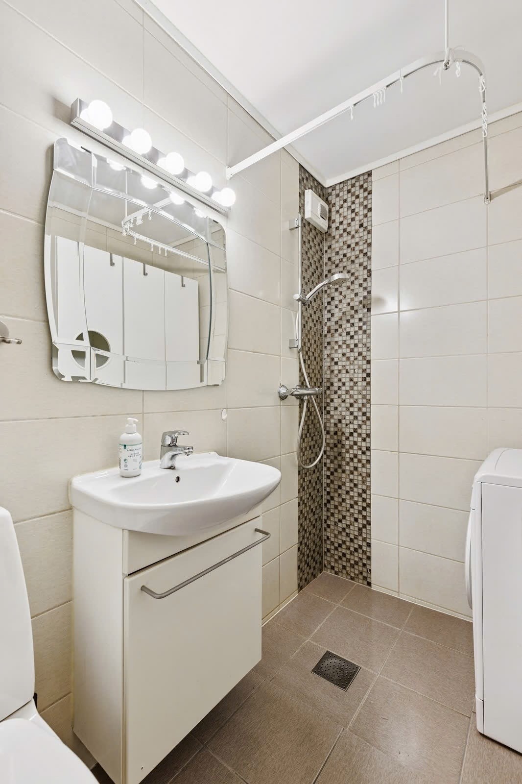 Pent flislagt bad med oppbevaring underservant i tillegg til skap rundt vaskemaskinen. Galleribilde