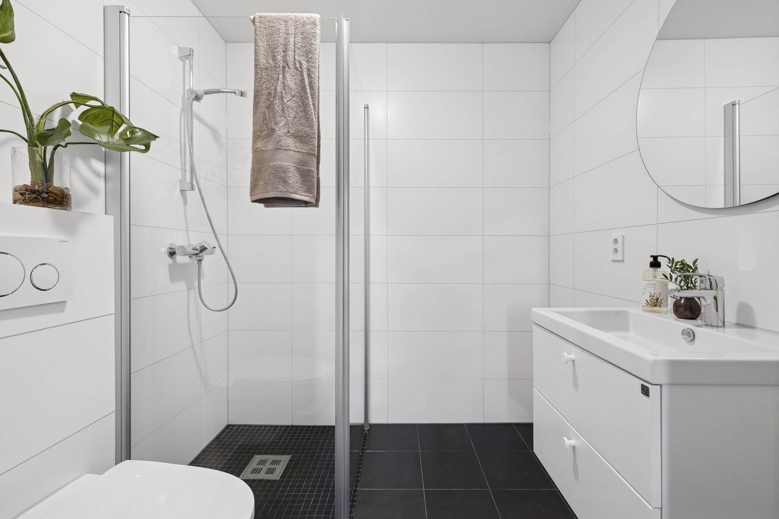 Baderommet er flislagt med elektriske varmekabler i gulv, utstyrt med vegghengt toalett, dusjhjørne med glassdører og baderomsinnredning med servant. Galleribilde