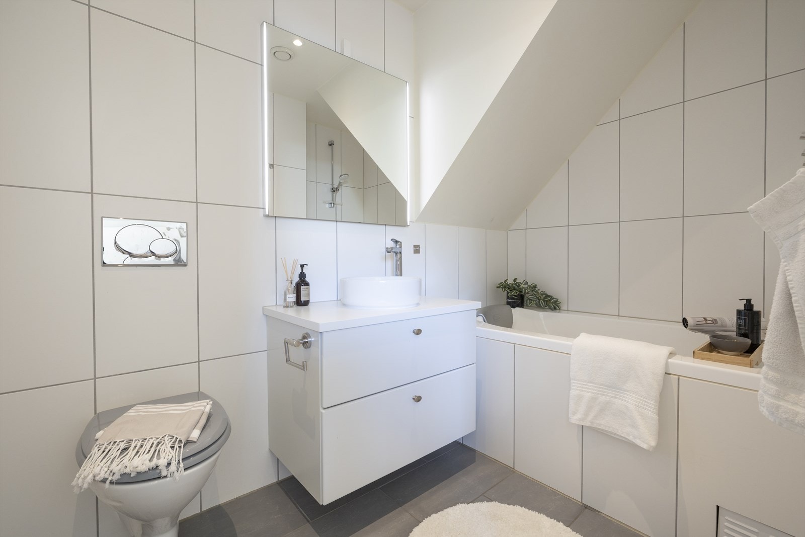 Badet i 2.etasje utstyrt med baderomsinnredning med servant, speil med lys, innmurt badekar og vegghengt toalett Galleribilde