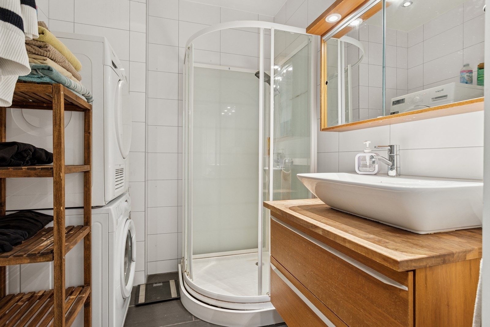 Flislagte vegger og gulv gir en solid og lettstelt overflate på badet. Dusjkabinett og vask med benkeplate i tre skaper en funksjonell våtromsløsning. Galleribilde