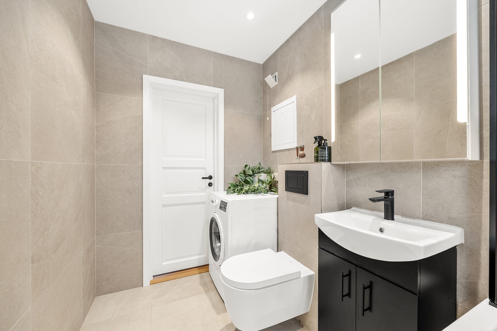 Baderomsinnredning med servant, vegghengt toalett og speilskap med integrert belysning. Galleribilde