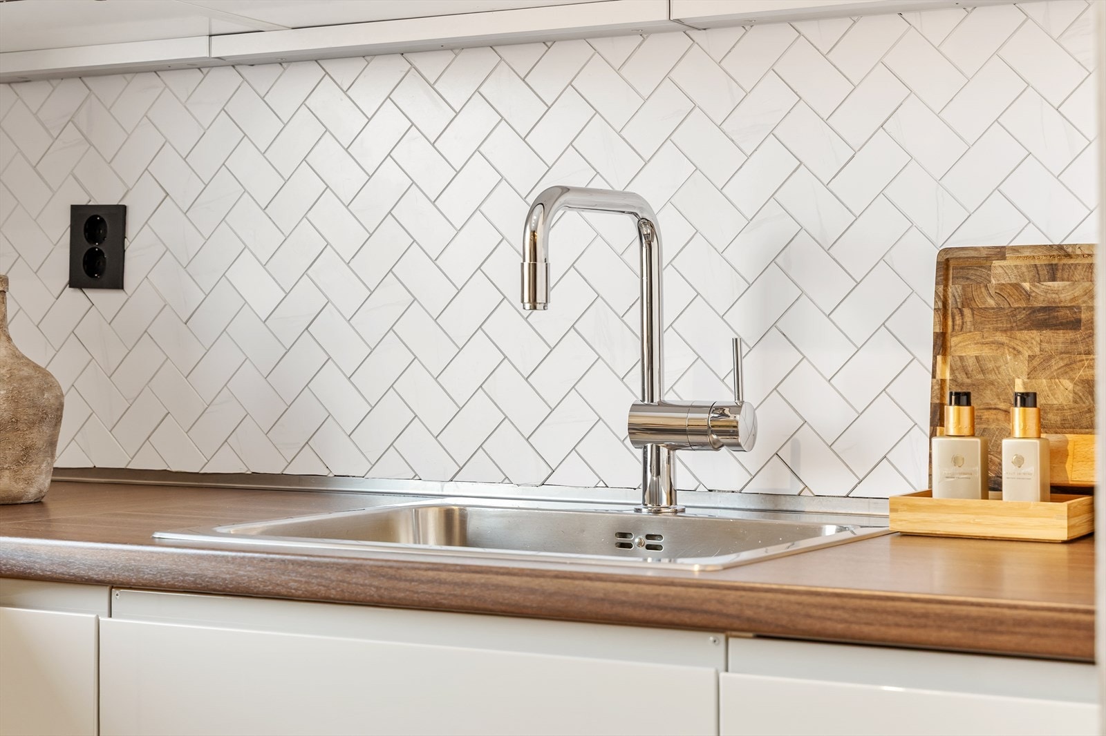 Fliser i fiskebeinsmønster over benken og et moderne blandebatteri er stilfulle detaljer. Galleribilde