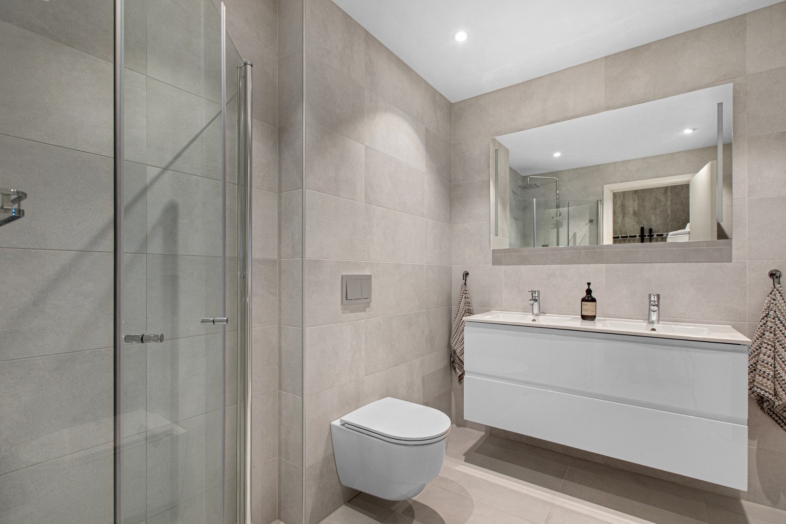 Et delikat og tidløst bad med dusjnisje og innfellbare glassdører, vegghengt toalett samt elegant servantinnredning. Galleribilde