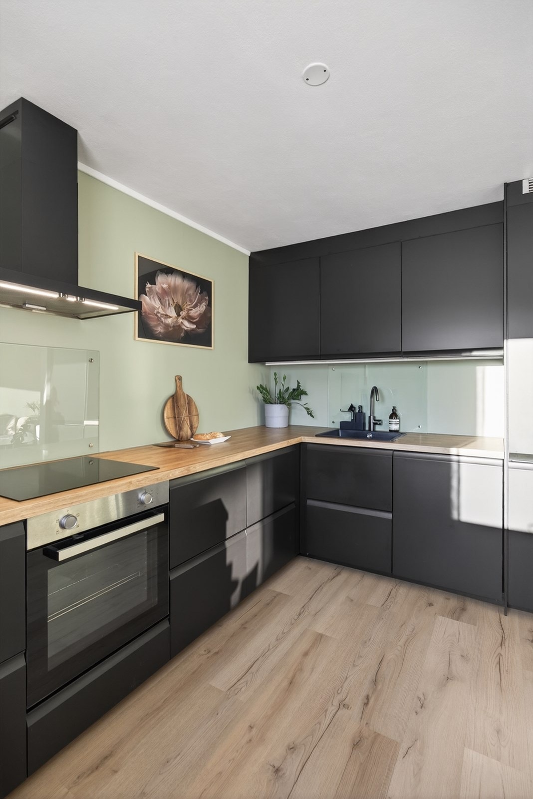 Benkeplate av eikemønstret laminat med sort nedfelt oppvaskkum gir kjøkkenet et moderne og gjennomført uttrykk. Galleribilde