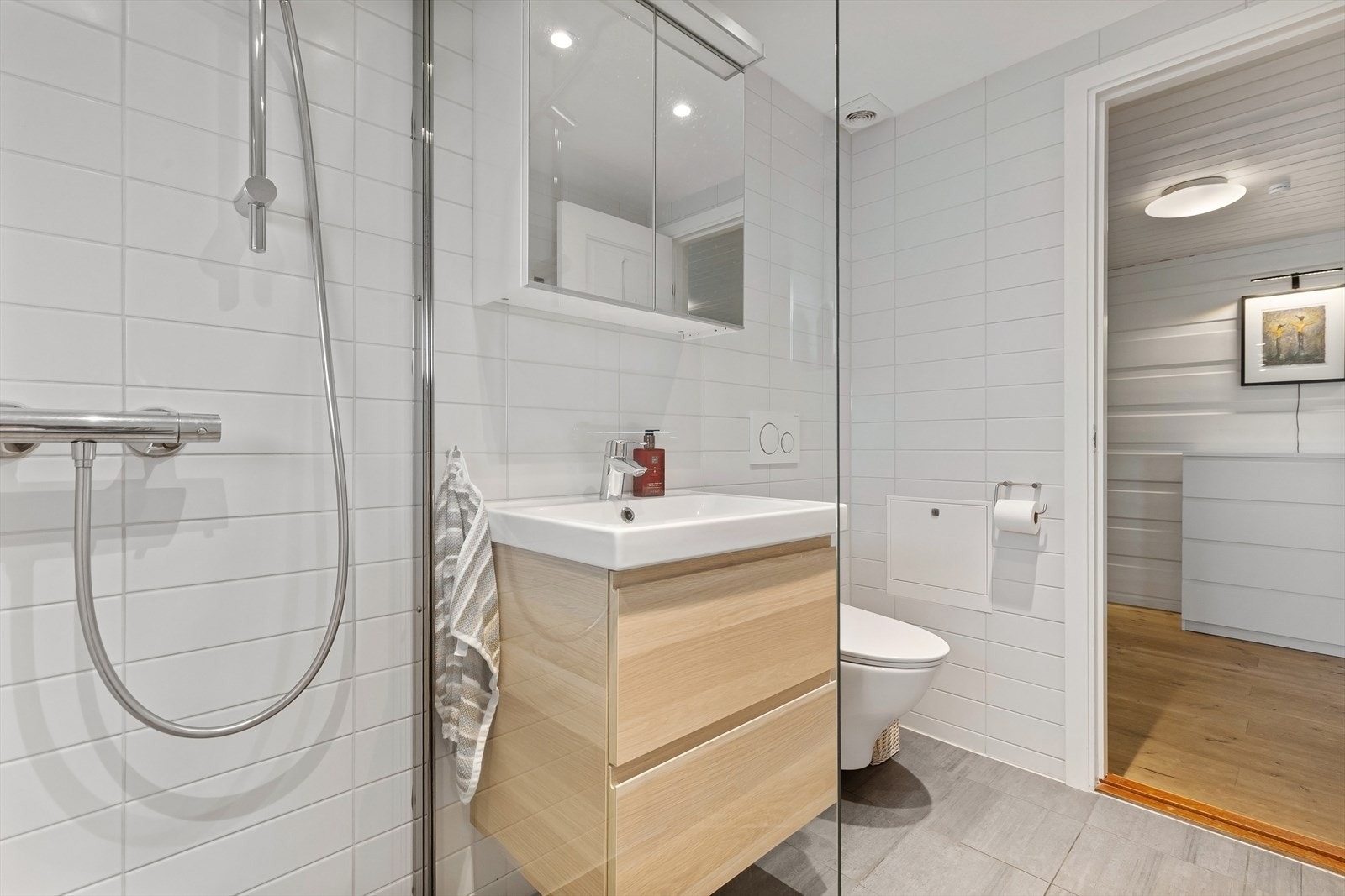 Badet er innredet med servant i innredning med to skuffer, speilskap, dusj med glassvegg og vegghengt toalett Galleribilde