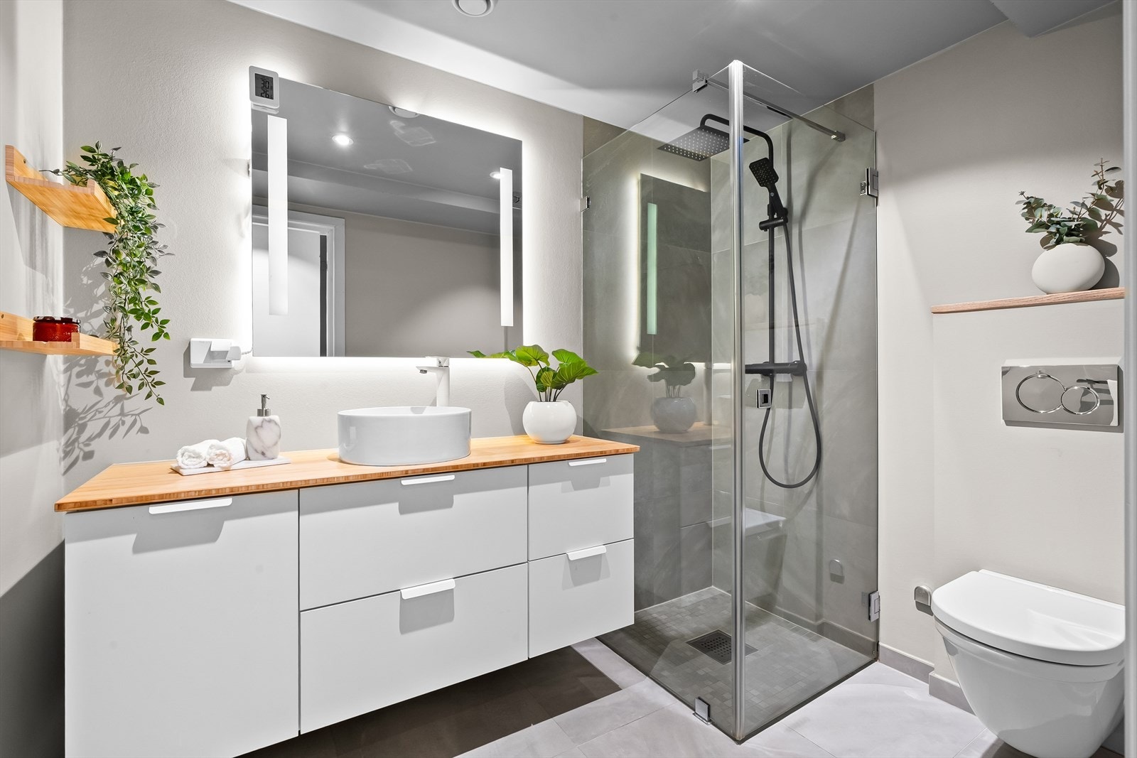 Lekkert, flislagt bad med elektrisk gulvvarme og downlights i himlingen. Badet har vegghengt klosett, servant med innredning, speil med integrert lys og dusjhjørne med svingbare glassdører. Galleribilde