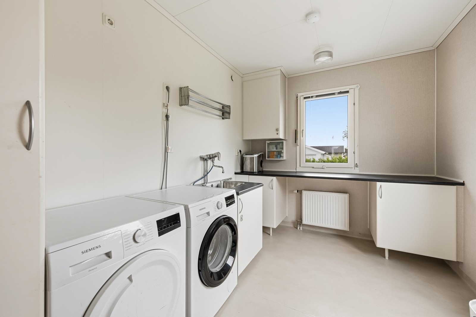 Praktisk vaskerom innenfor kjøkkenet med egen utgang. Rommet har skap- og benkeinnredning, utslagsvask og opplegg for både vaskemaskin og tørketrommel. Galleribilde