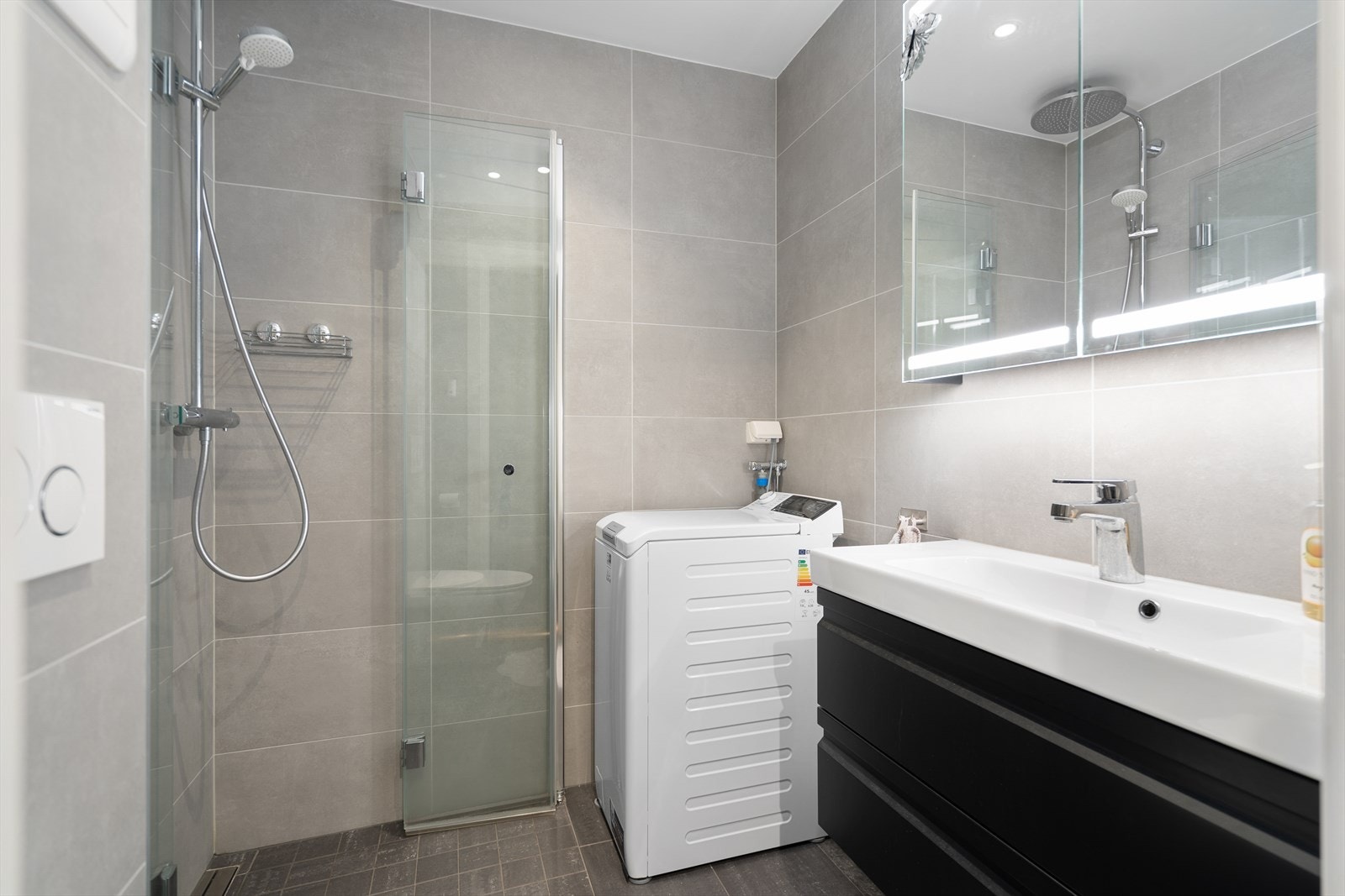 Moderne baderom med lyse fliser, dusjhjørne og plass til vaskemaskin - et tidløst og funksjonelt rom Galleribilde