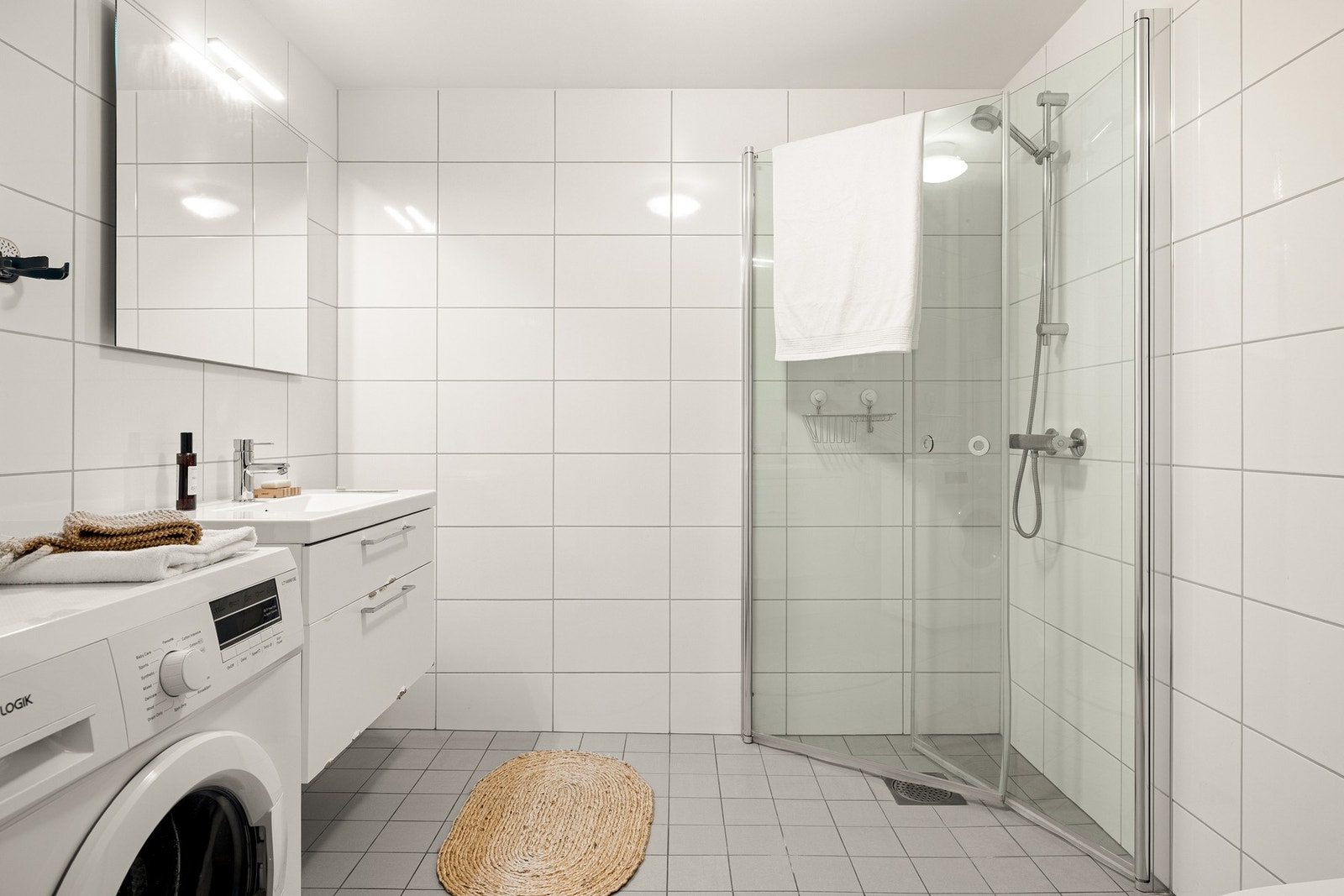 Det er innredet med vegghengt toalett, dusj med glassvegger og baderomsinnredning med speil og belysning Galleribilde