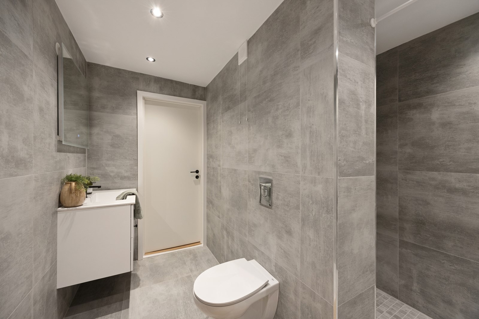 Innredningen inkluderer veggmontert toalett, servant med underskap og opplegg for vaskemaskin. Galleribilde