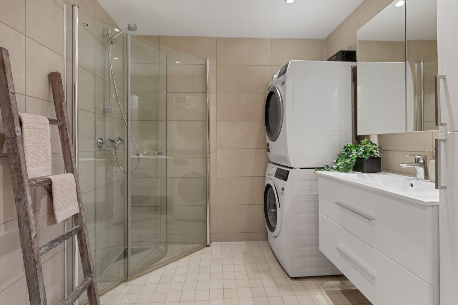 Det stilige, flislagte baderommet har varmekabler i gulvet for ekstra komfort. Badet er elegant innredet med vegghengt toalett, servantinnredning med speilskap, samt et dusjhjørne med innfellbare glassdører. Galleribilde