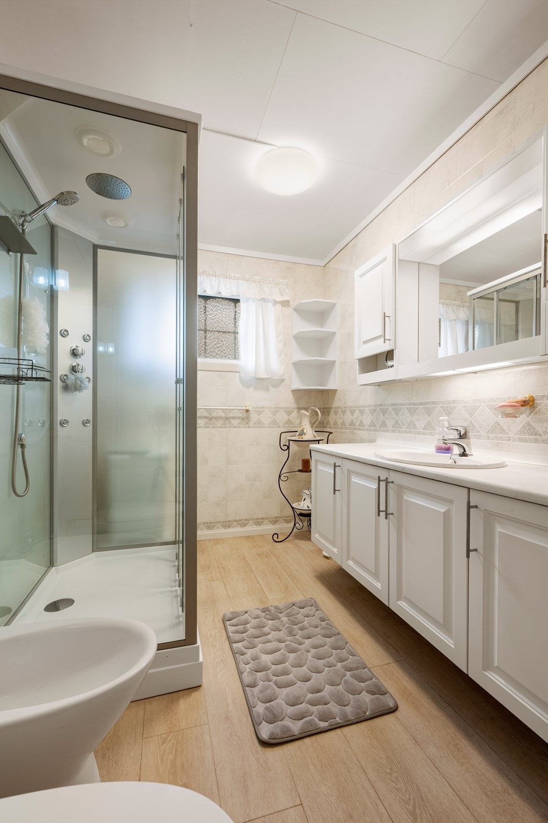 Badet er utstyrt med dusjkabinett, servant med tilhørende skap, wc og bidé Galleribilde