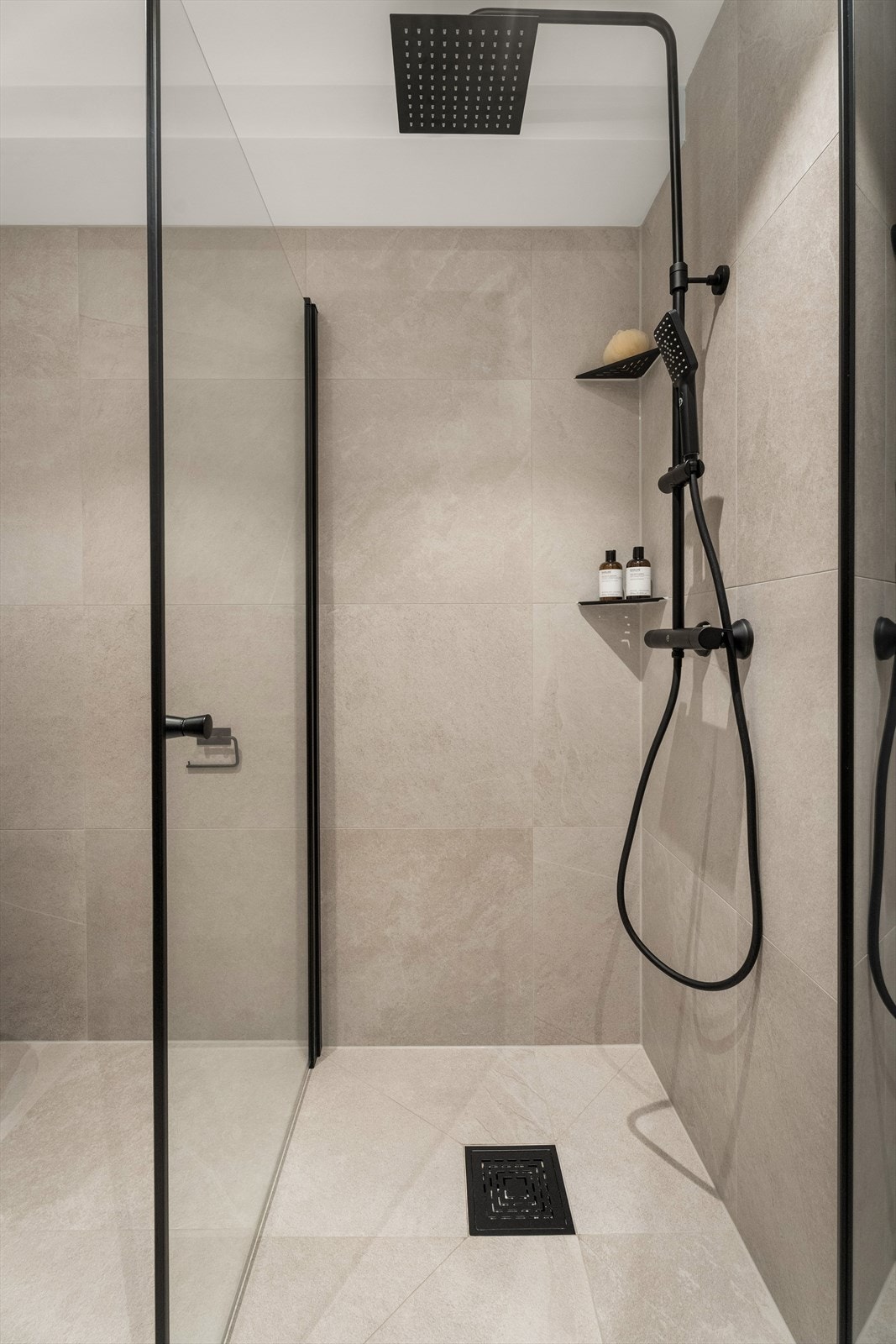 Baderommet er innredet med en stilren servantinnredning, vegghengt toalett, et dusjhjørne med glassdører og et praktisk oppbevaringsskap. Galleribilde