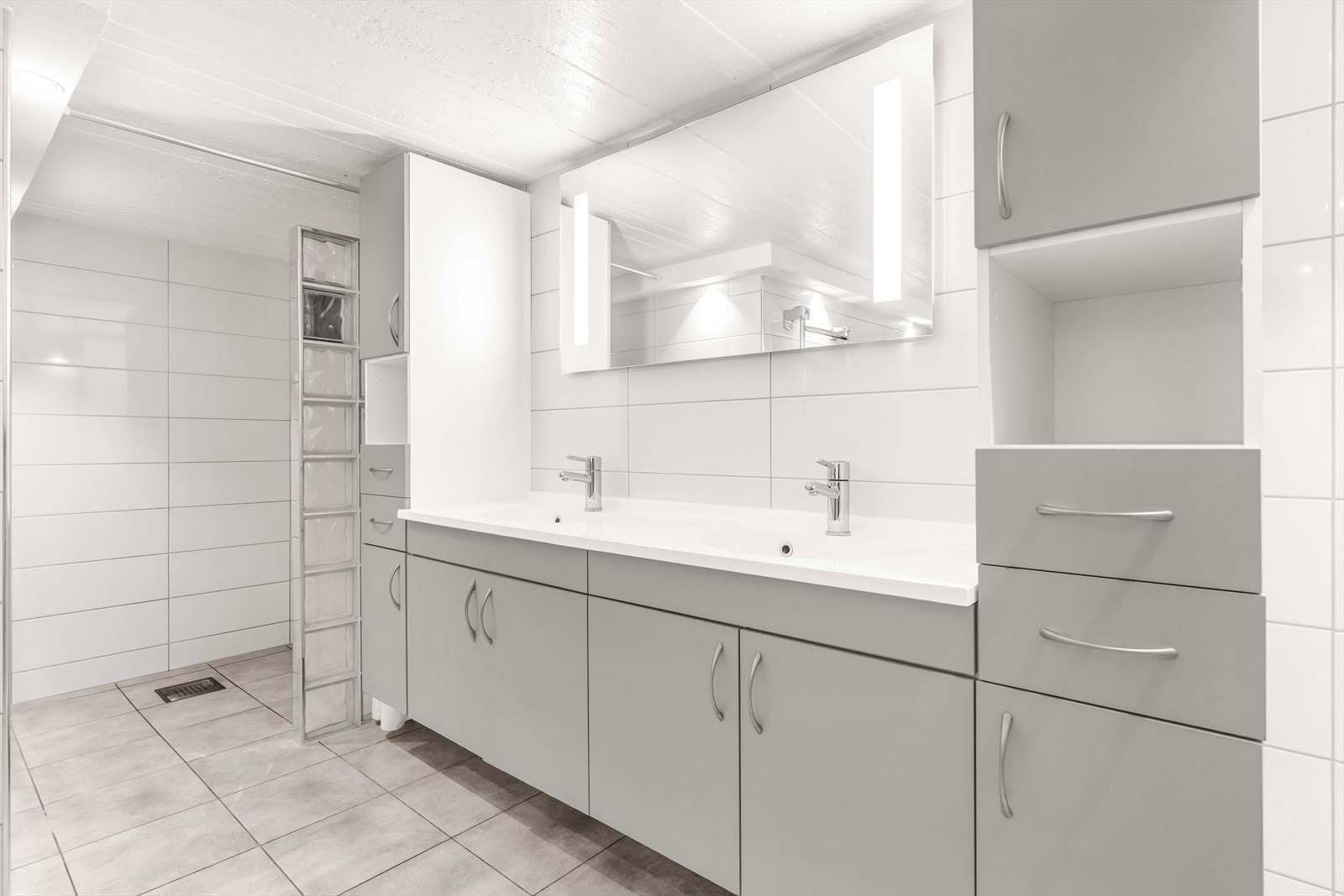 Rommet er innredet med dobbel servant og dusj. Det er rikelig med oppbevaring i grå, glatt innredning. Galleribilde