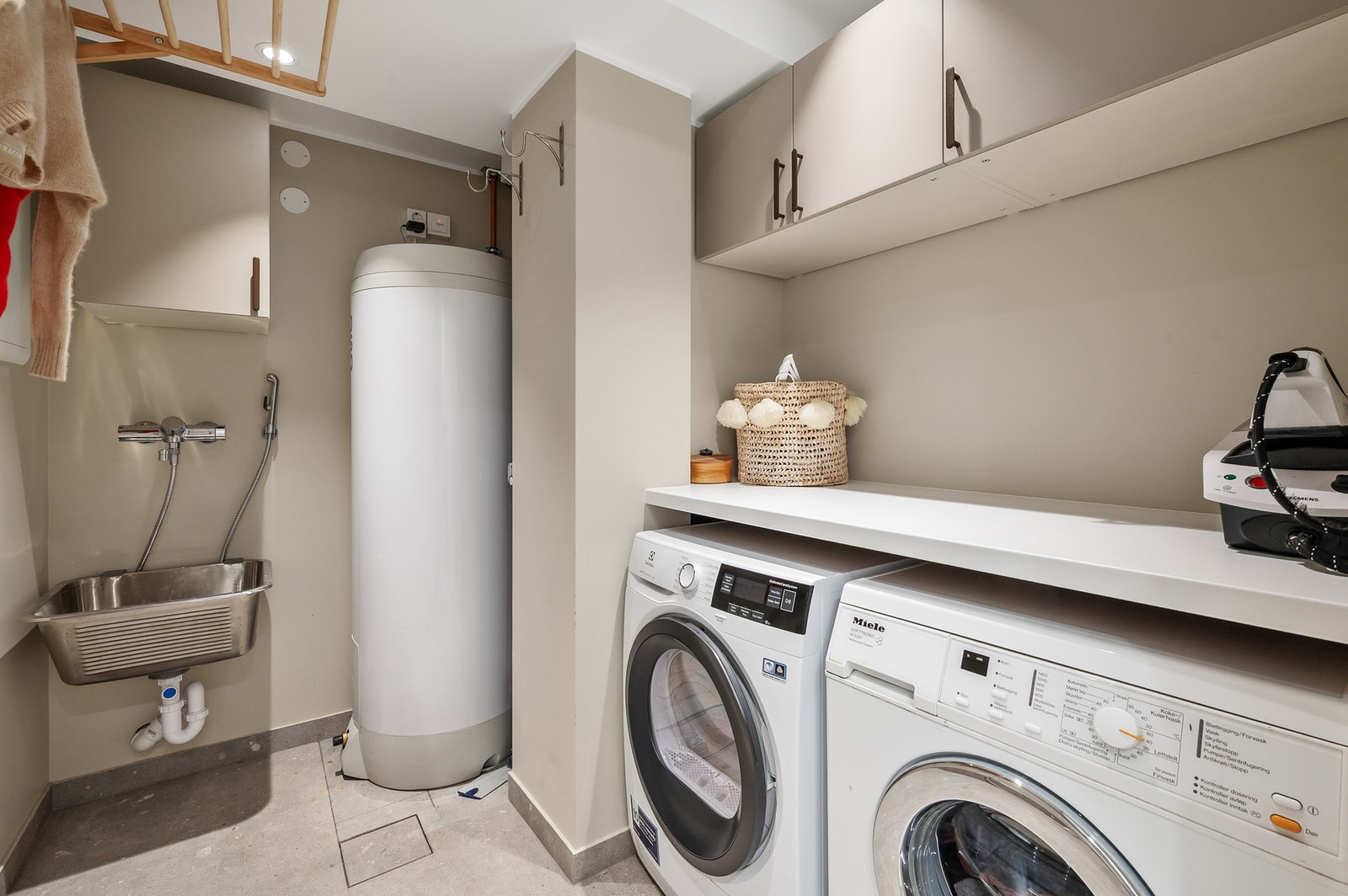 Vaskerom fra 2022. Rommet er innredet med benkeløsning, skap, utslagsvask med ett-greps armatur samt opplegg for vaskemaskin og tørketrommel med stikkontakter under benk. Galleribilde