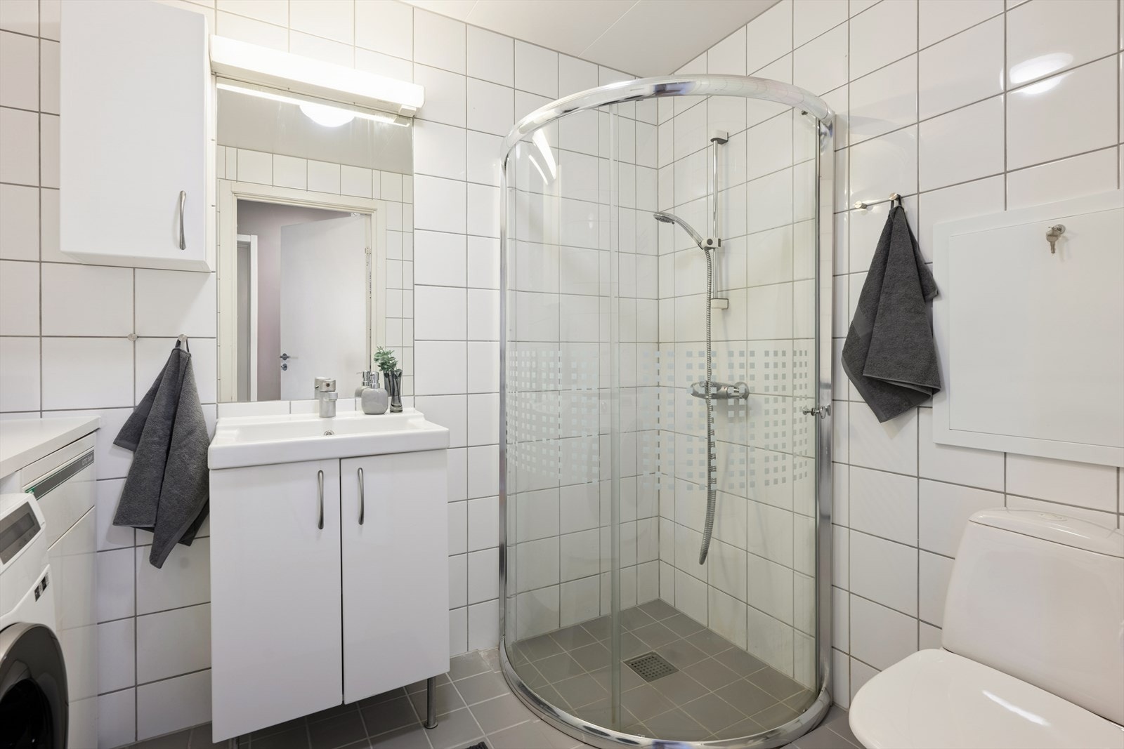 Rommet er innredet med romslig dusjsone, baderomsinnredning, toalett, belyst speil og veggmontert skap. Galleribilde