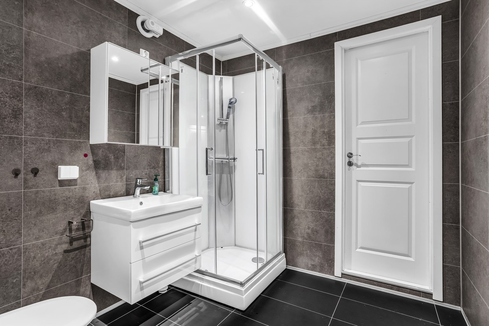 Badet i underetasjen er flislagt og utstyrt med dusjkabinett og servant med oppbevaring. Galleribilde