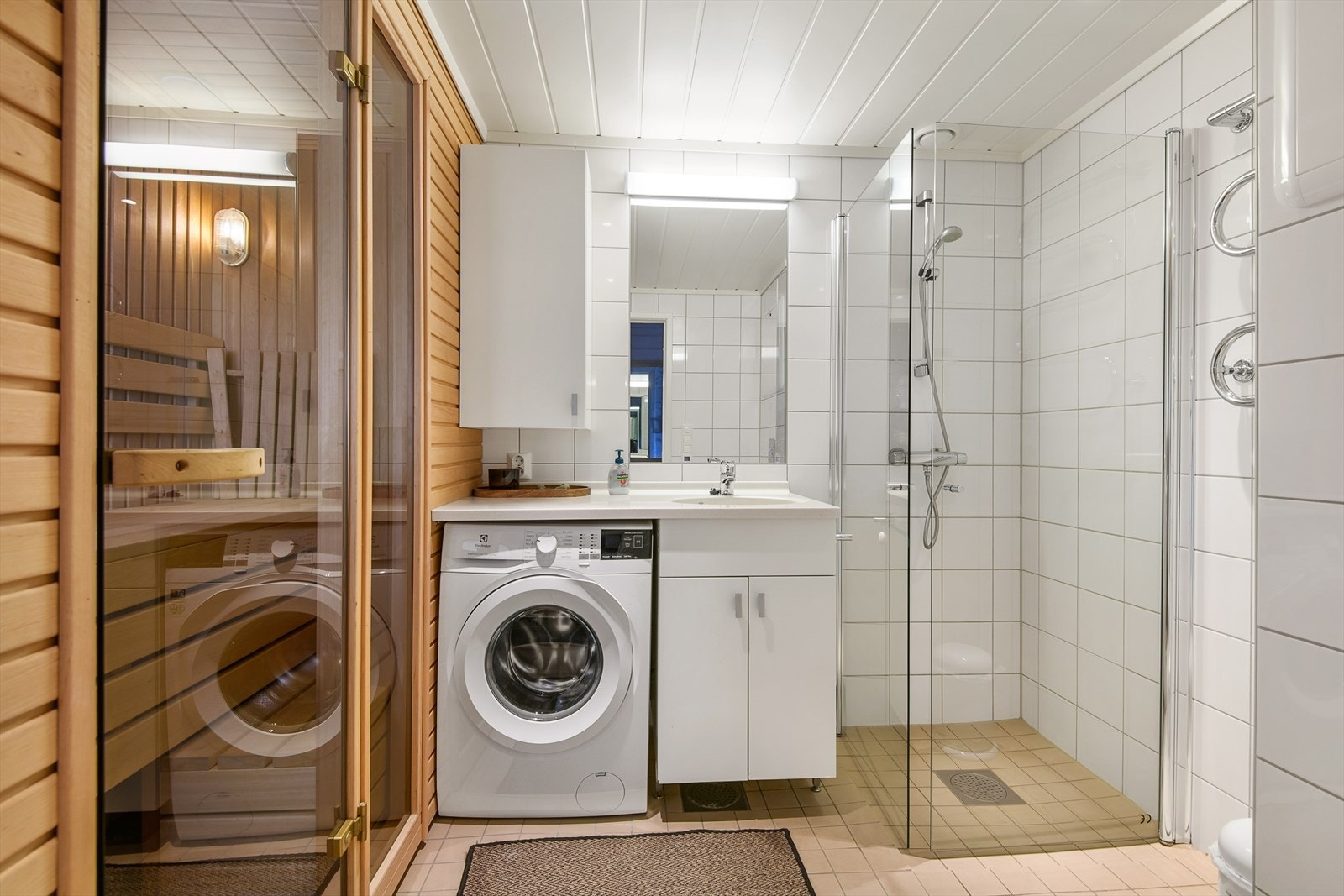 Tidløst og meget funksjonelt bad/wc med dusj, servantinnredning, opplegg for vaskmasking og badstue. Galleribilde