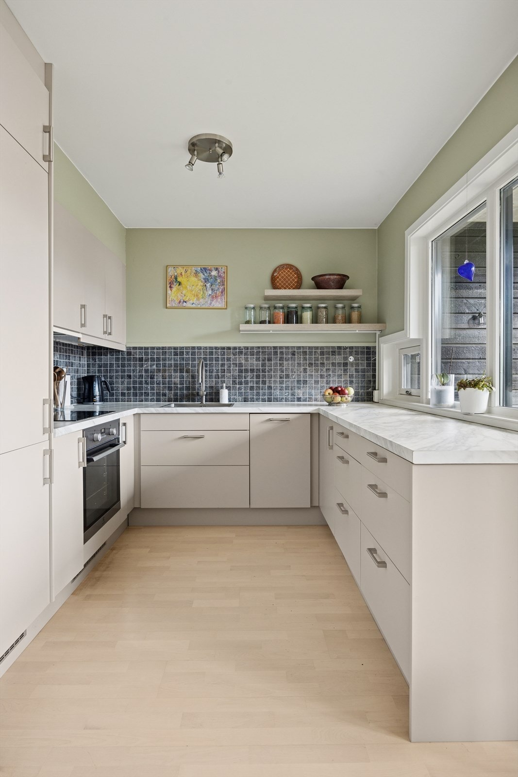 Kjøkkenet er plassert i egen sone og har innredning med malte glatte fronter, stål håndtak og en lekker benkeplate i laminat som gir et moderne uttrykk. Galleribilde