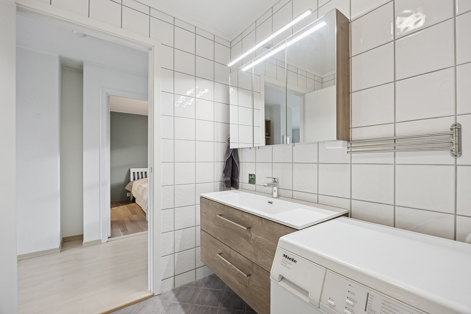 Badet er utstyrt med skapinnredning, gulvmontert toalett, dusjhjørne med innfellbare glassdører og servant med ettgreps blandebatteri. Galleribilde