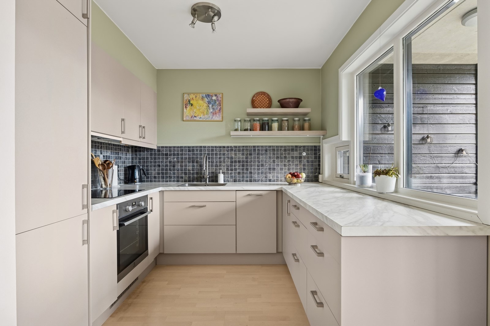 Kjøkkenet er innredet med moderne, glatte fronter og en benkeplate i laminat som gir et tidløst og innbydende uttrykk. Galleribilde