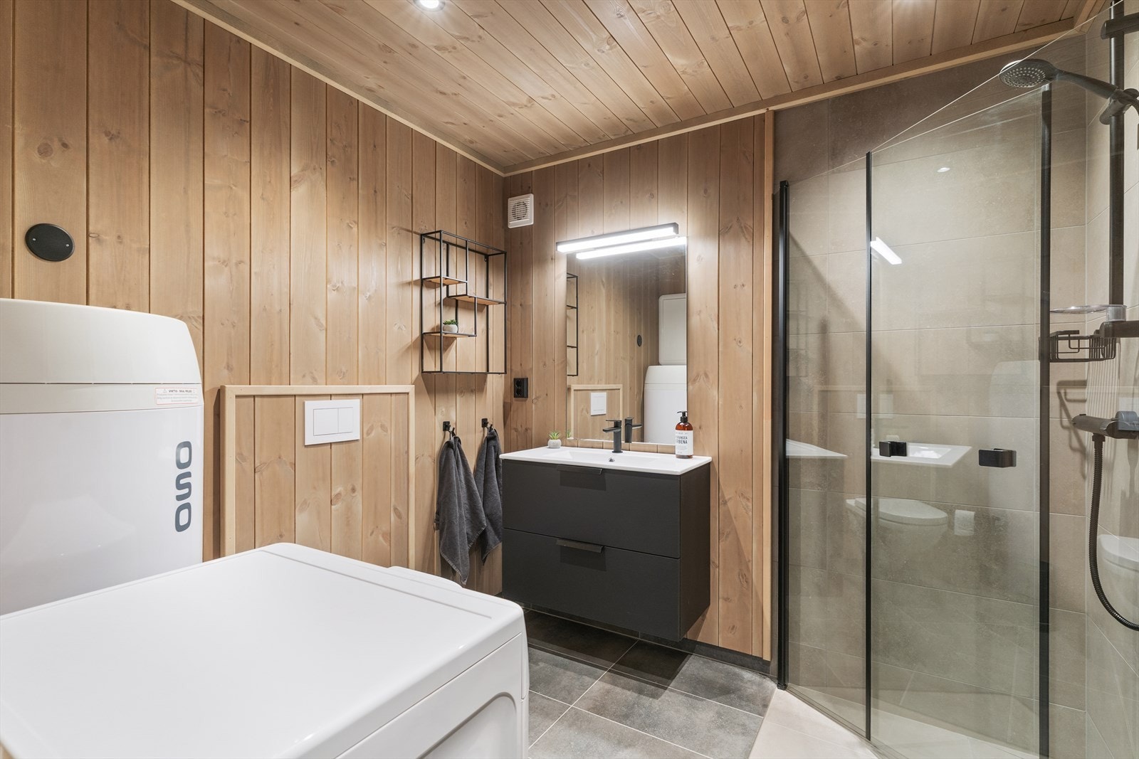 Bad/vaskerom. Også med flis på golv med varmekablar. Vegghengt toalett, dusjsone med innfellbare dører og skuffeinnreiing med servant. Galleribilde