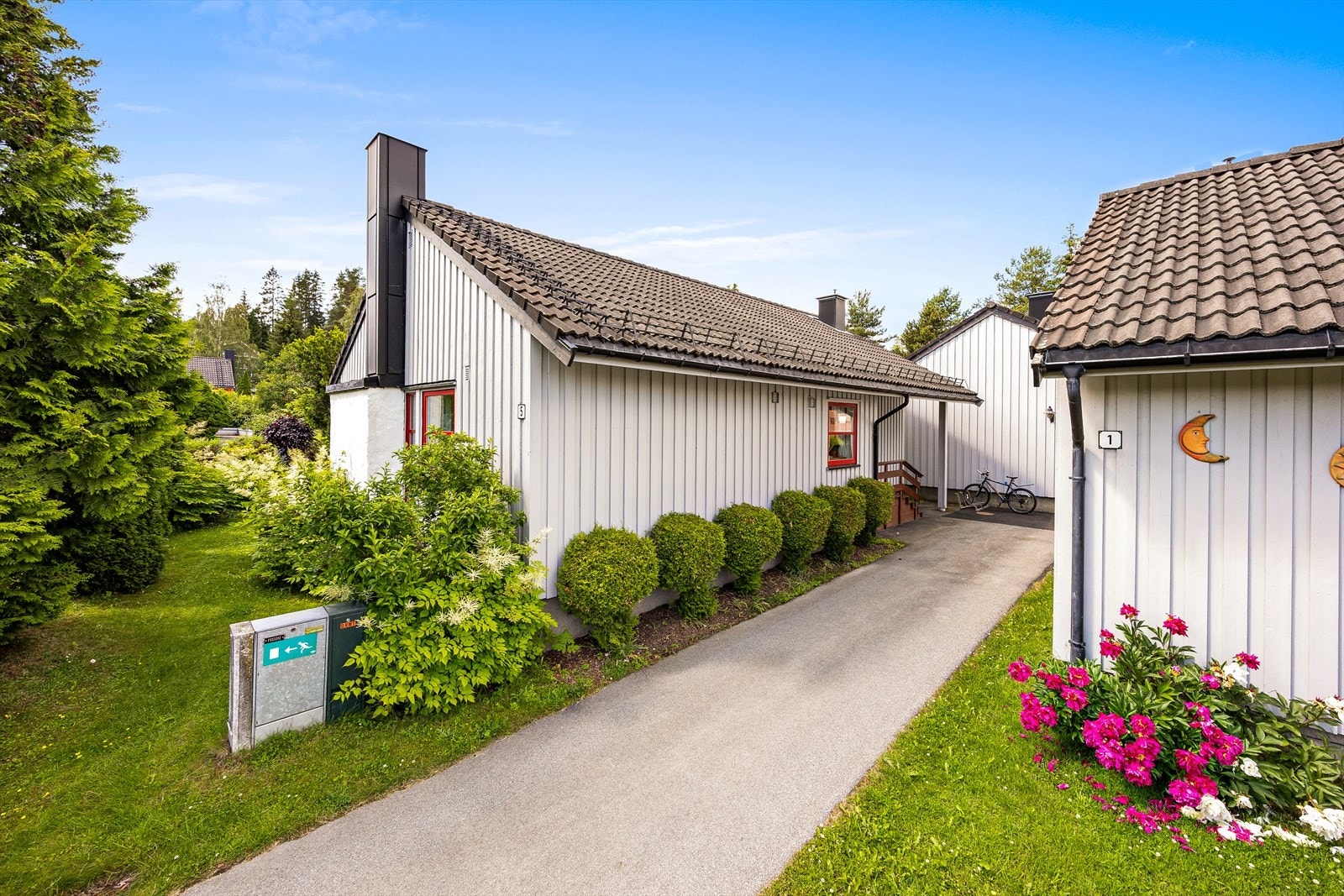 Inngangsparti flankert av velstelte busker og blomster for en innbydende ankomst til hjemmet. Galleribilde