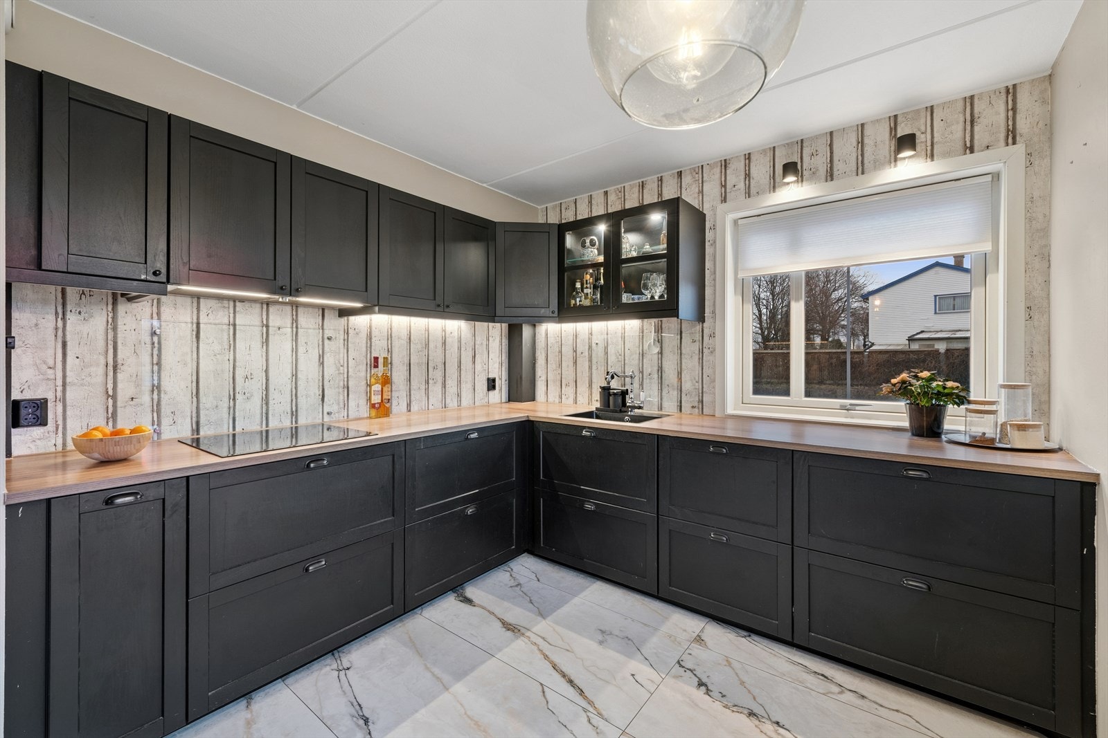 Laminerte benkeplater i treimitasjon skaper en varm kontrast til de mørke frontene, mens integrert benkebelysning gir både funksjonelt arbeidslys og en lun stemning. Galleribilde