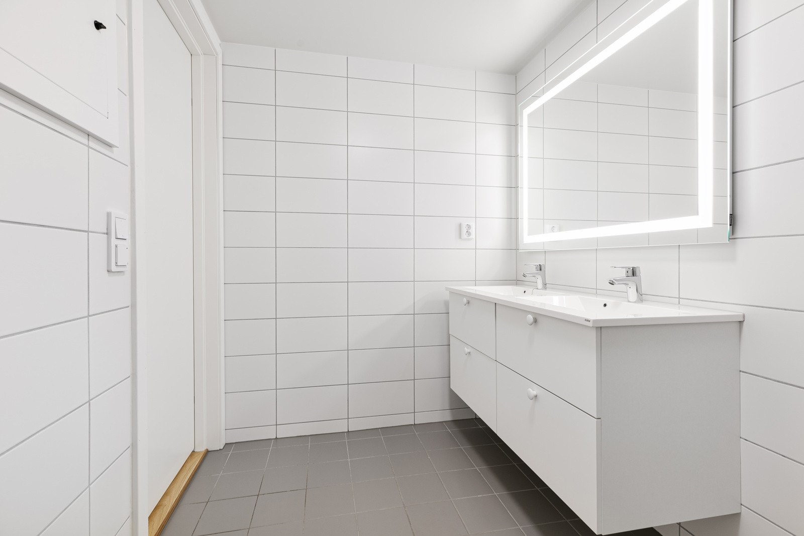 Badet er innredet med dusjhjørne, veggmontert toalett og dobbel servant Galleribilde