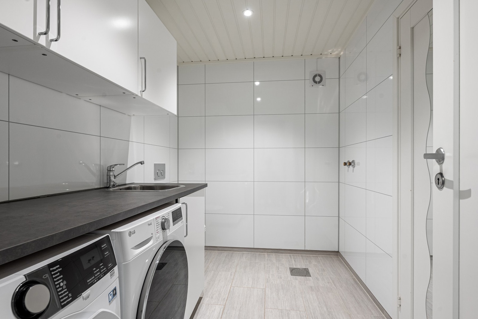 Praktisk vaskerom med flislagt gulv og gulvvarme. Det er opplegg for dusj med sluk i gulvet. Galleribilde