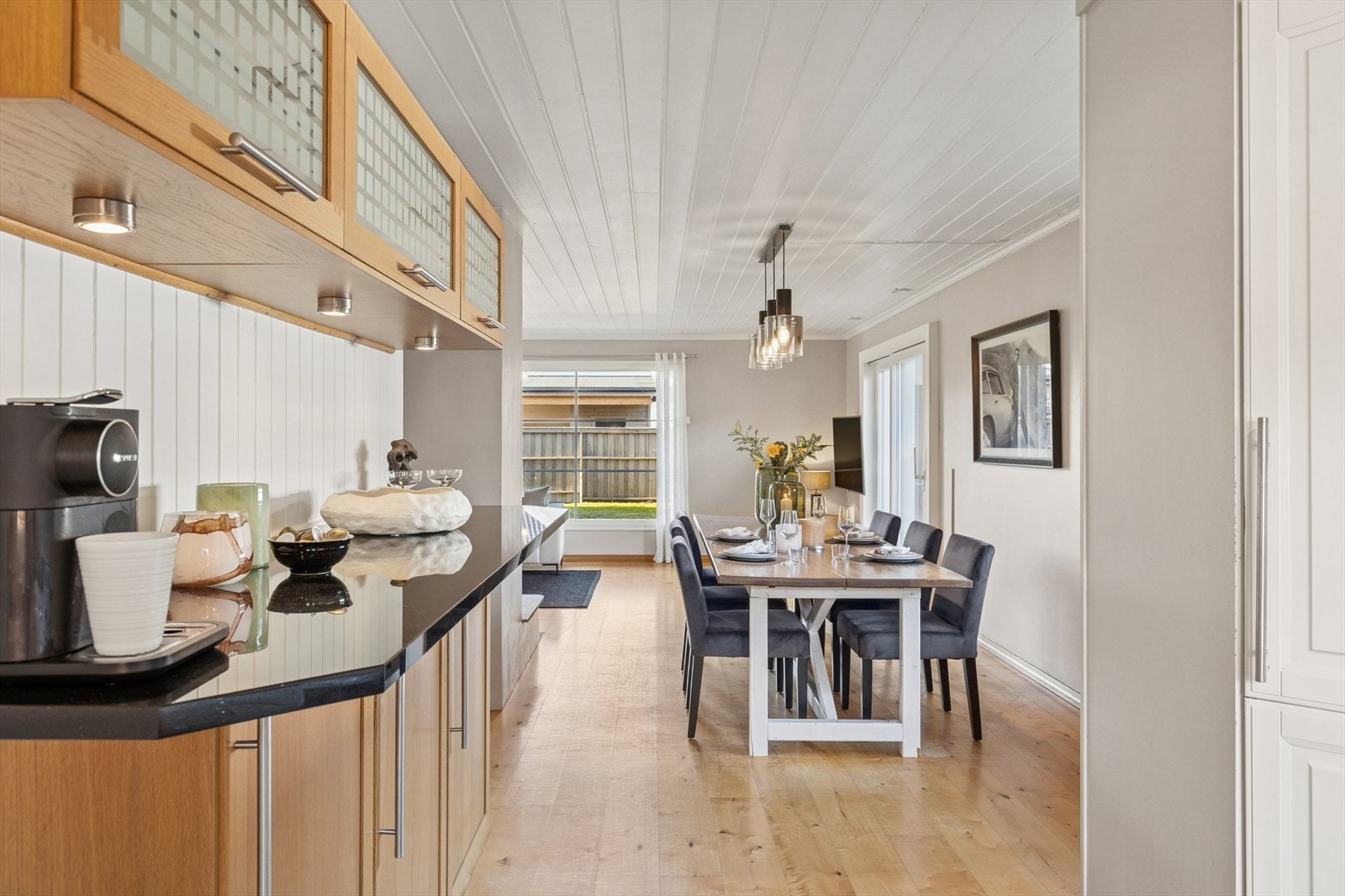 I sonen mellom kjøkkenet og spisestuen er det laget en innredning med brune, profilerte fronter og sort benkeplate, samt overskap med glassdører. Galleribilde