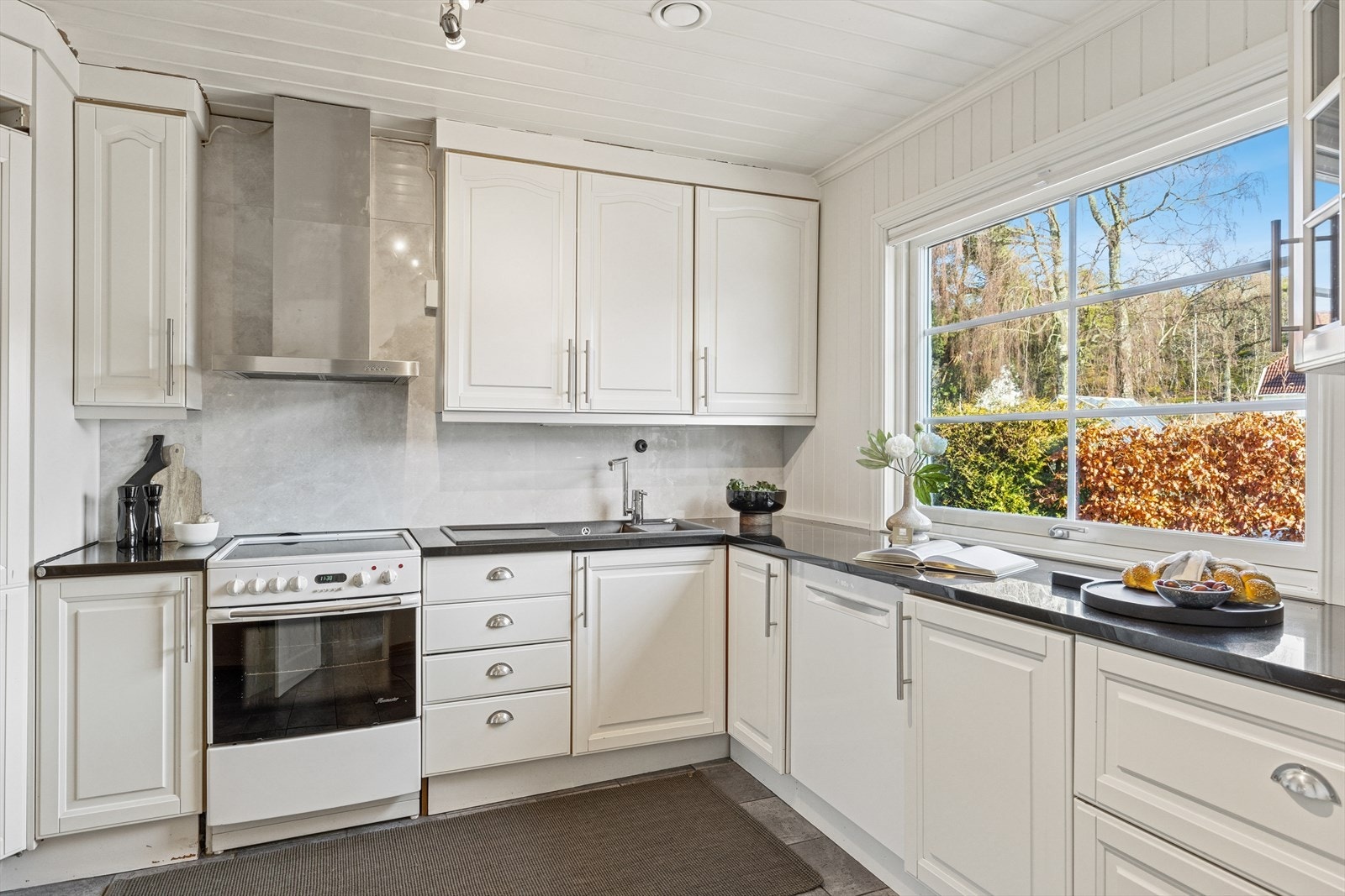 Kjøkkeninnredningen er av eldre dato og er pent utført med hvite, profilerte fronter og mørk benkeplate i stein med oppvaskkum i komposittmateriale med utslagsvask. Galleribilde