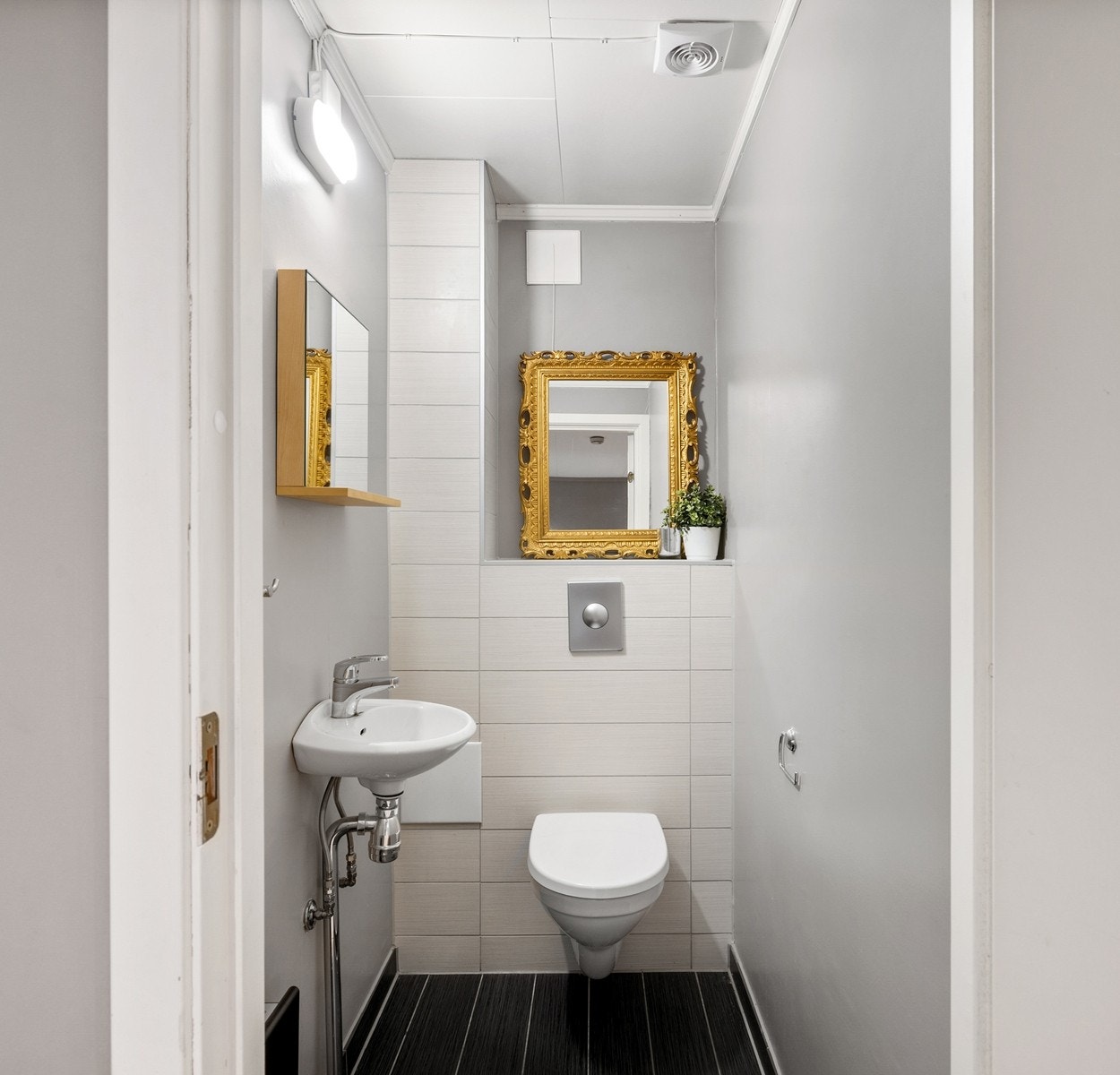 Toalettrom med vegghengt toalett og liten servant gir rommet et luftig preg, mens det mørke, flislagte gulvet med gulvvarme og de lyse veggflisene skaper en elegant kontrast. Praktisk plassert like ved entréen. Galleribilde