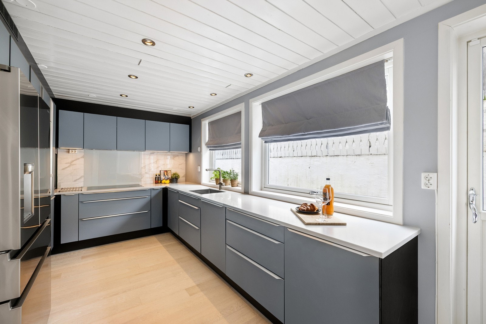 De stilrene, blågrå frontene med integrerte håndtak gir et tidløst uttrykk, med hvit composit benkeplate og matchende fliser i marmormønster skaper et eksklusivt preg. Galleribilde