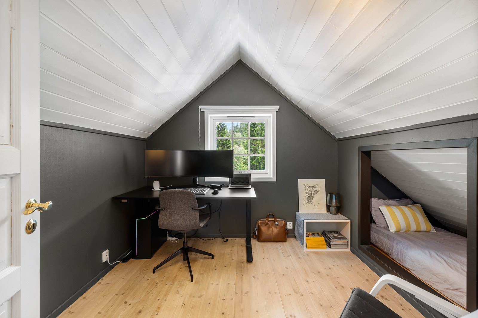 Rommet er innredet med et moderne hjemmekontor med en stilfull, mørk kontrastvegg og skråtak som gir rommet karakter. En smart innebygd sovealkove med plassbygget seng gir ekstra soveplass. Galleribilde
