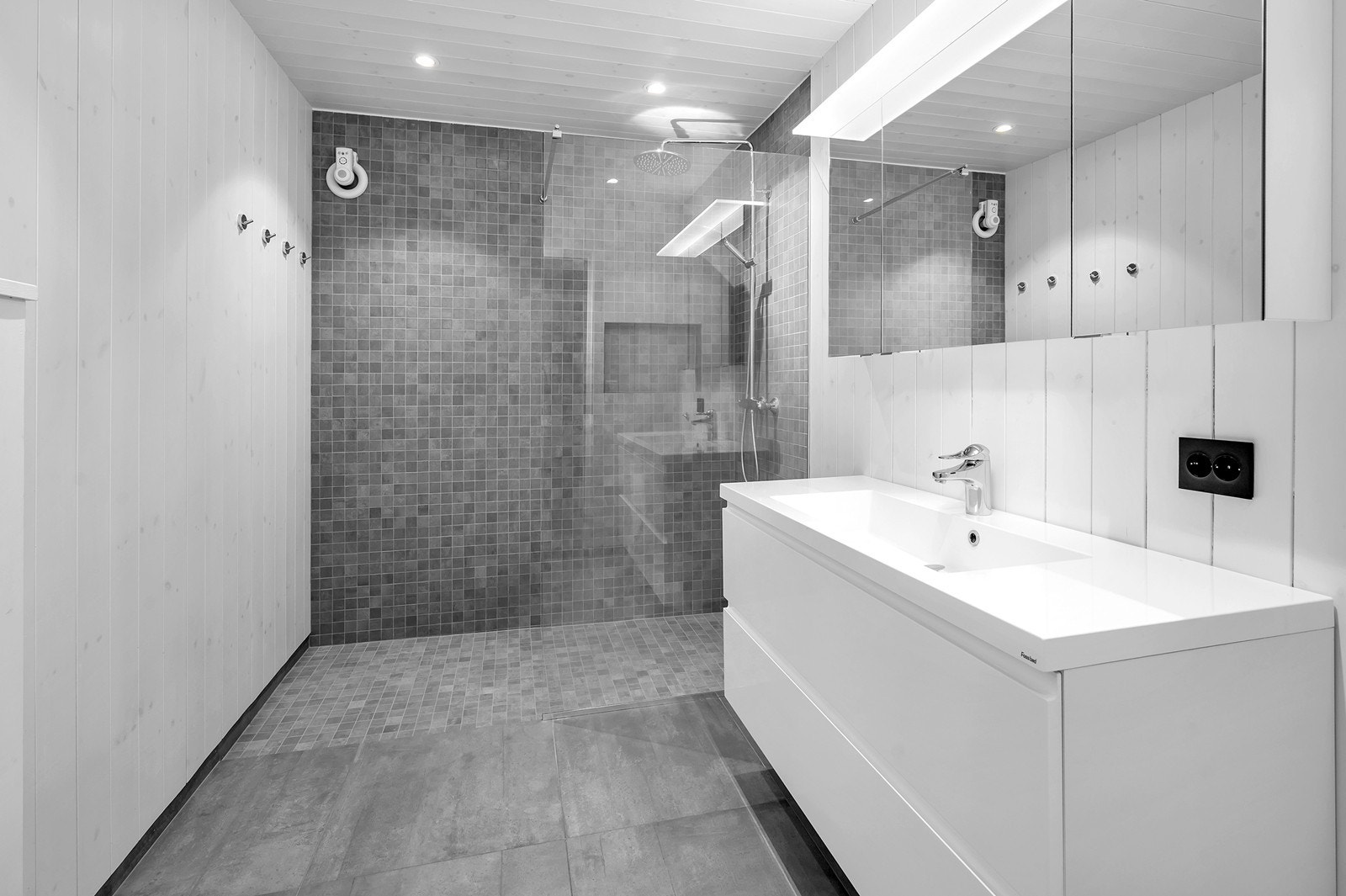 Flislagt bad med stor dusjnisje, servant med skuffer, vegghengt toalett og speilskap. Galleribilde