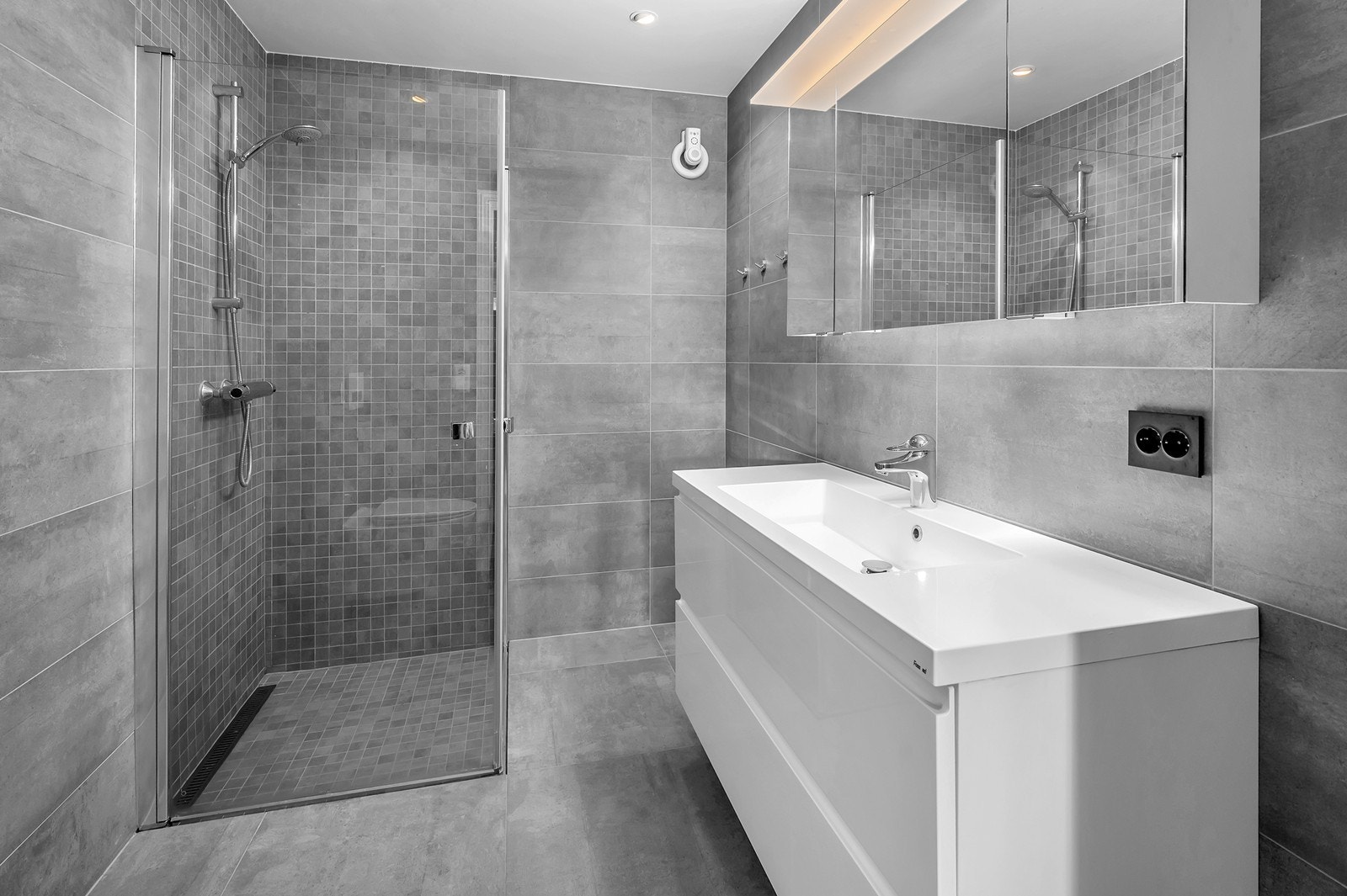 Flislagt bad i underetasjen med dusjnisje, servant med skuffer, vegghengt toalett og speilskap. Galleribilde